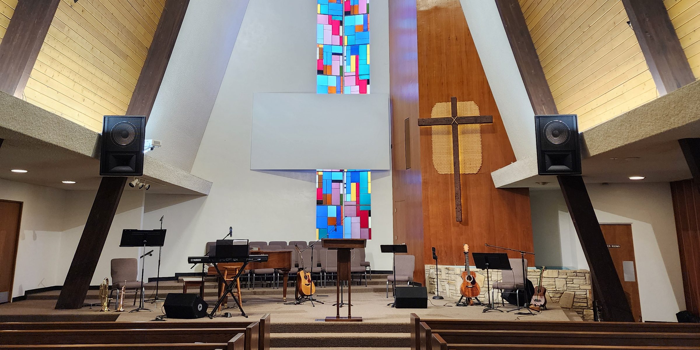 Sanctuary of Rosedale Bible Church with wooden pews, a tall stained-glass window, and a cross on the front wall